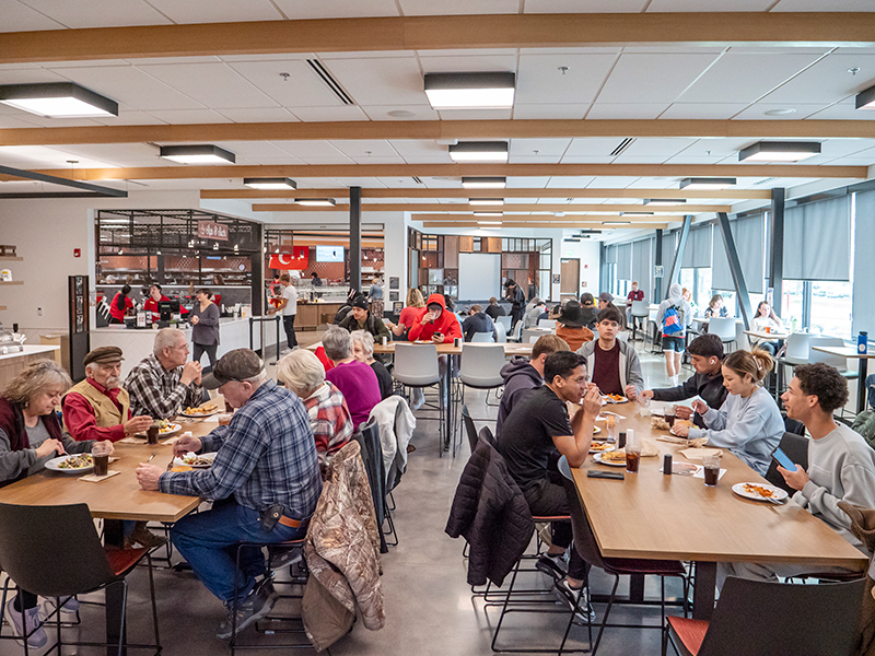 A goup of people sitting around tables and eating lunch in the college dining hall