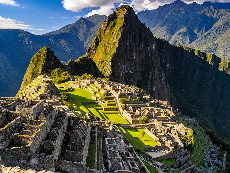 Aerial view of Machu Picchu at sunrise in the Andes Mountains with partially shadowed ruins below a mountain peak