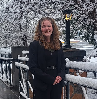 Lauren Bates standing on a snow-covered bridge with a small street light and trees behind her