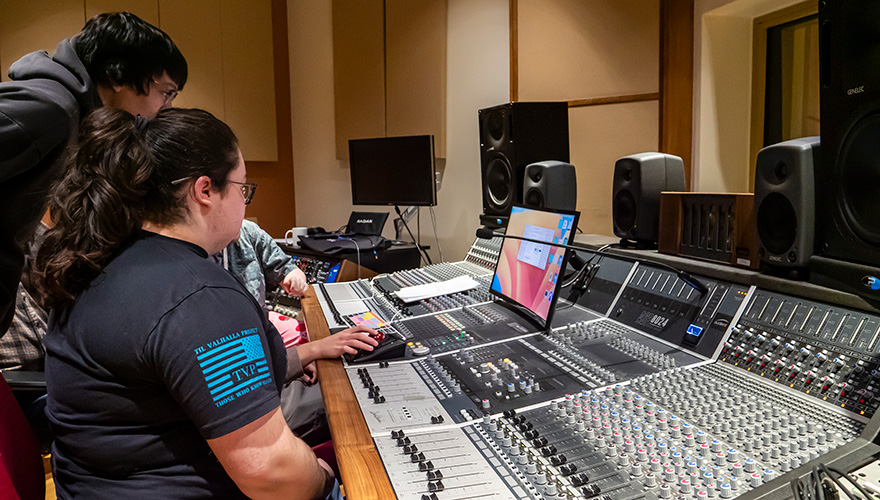 A group of three students sitting at a control board inside a studio