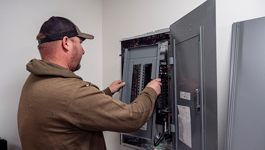 A man in a baseball cap and brown hoodie opening an electrical panel