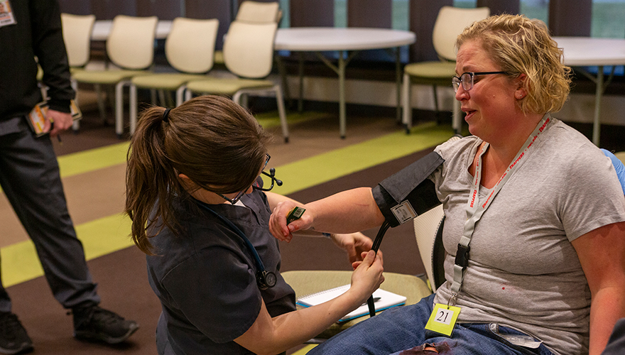 A female nursing student checking the blood pressure of a female patient sitting in a chair