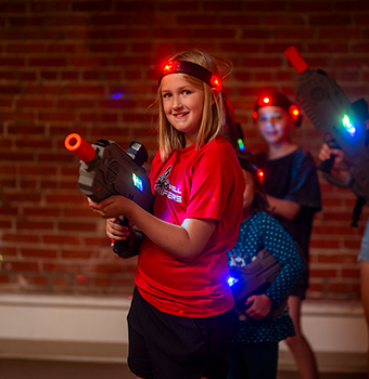 A young girl playing laser tag in a dim room with brick walls