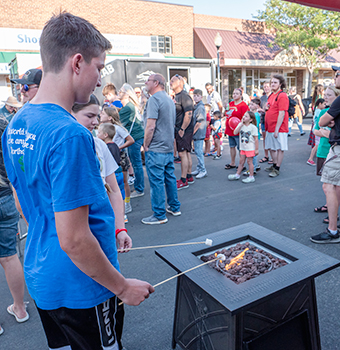 A young male and female roasting marshmallows over a firepit on a crowded street