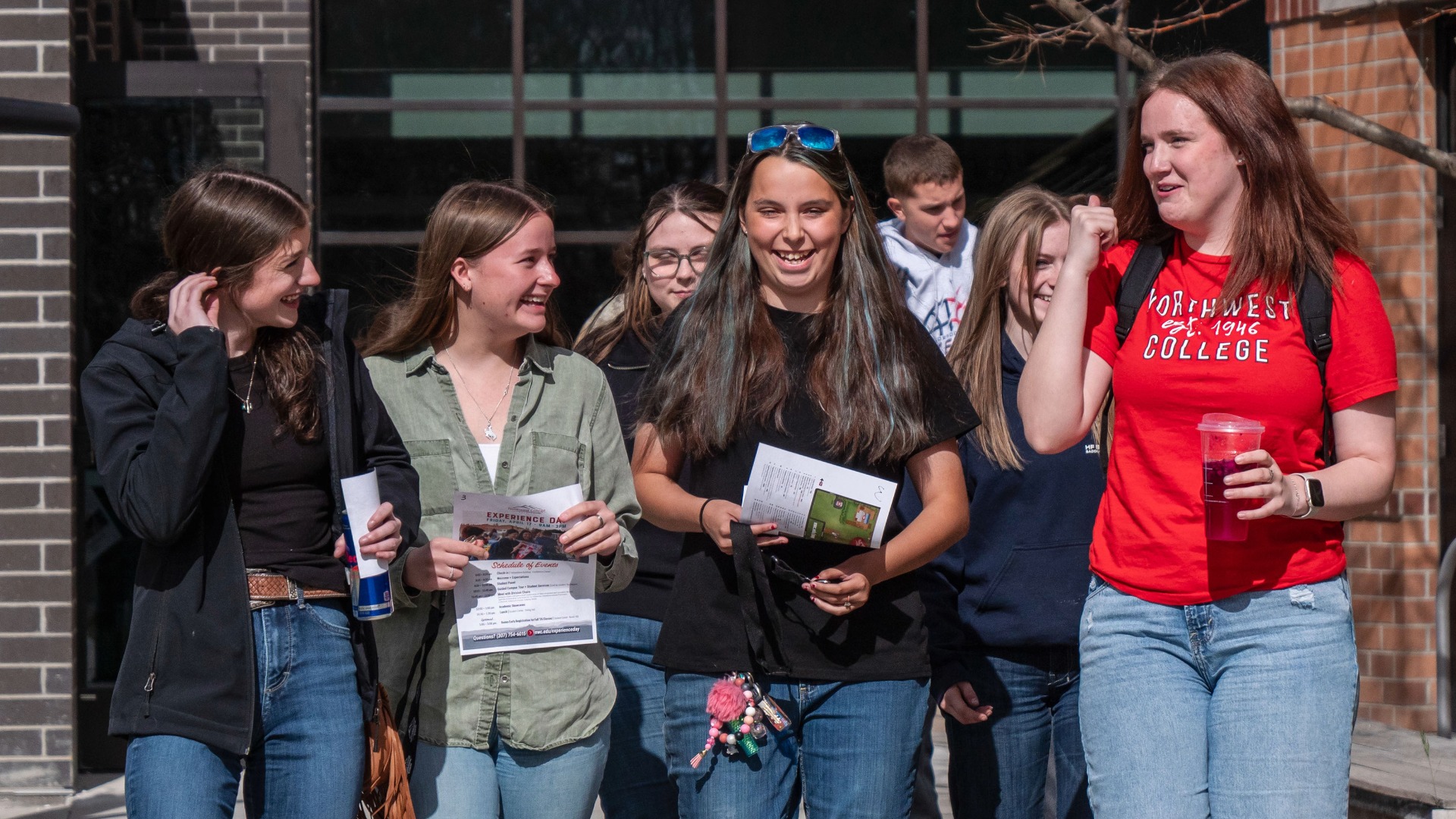 A group of high school students walking down a sidewalk toward the camera being led by a college student
