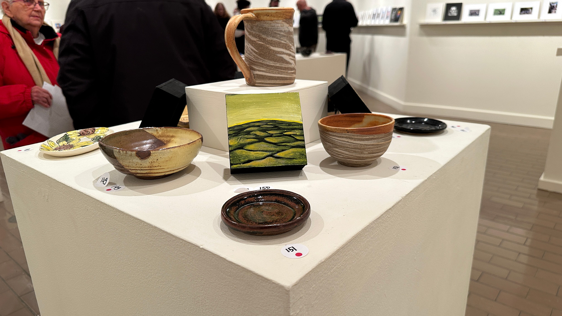 A collection of ceramic art work on a stand inside an art gallery with people in the background