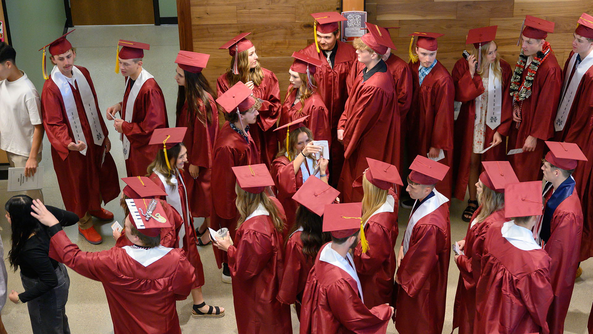 An view looking down from the second floor at a group of graduates in red robes talking and lining up on the first floor