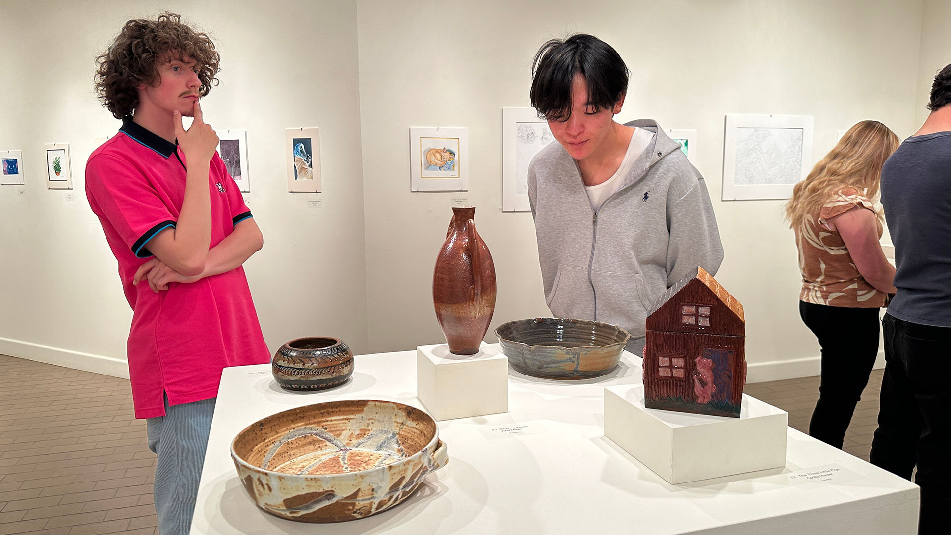 Two male college students looking at ceramics on a square table inside a gallery