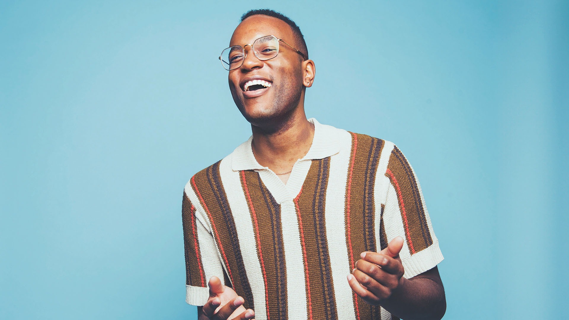 A laughing man wearing glasses and holding his hands out in front of him