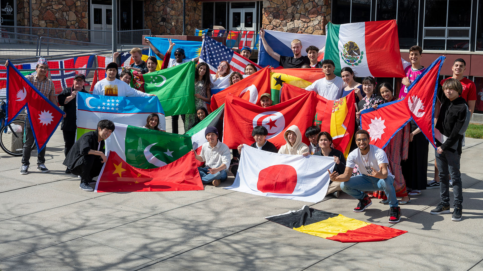 A large group of international students holding flags from different countries outside a building