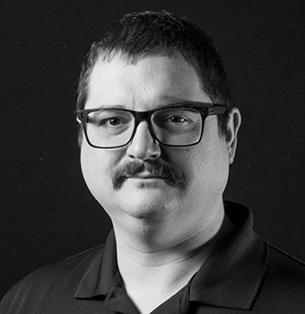A black and white portrait of a man with glasses and a mustache wearing a dark shirt