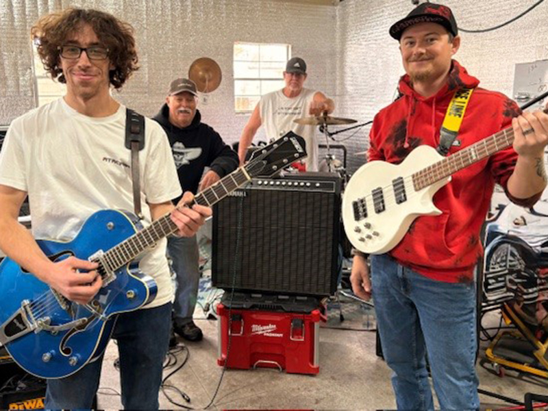 A group of four male band members holding or sitting with instruemnts in a studio