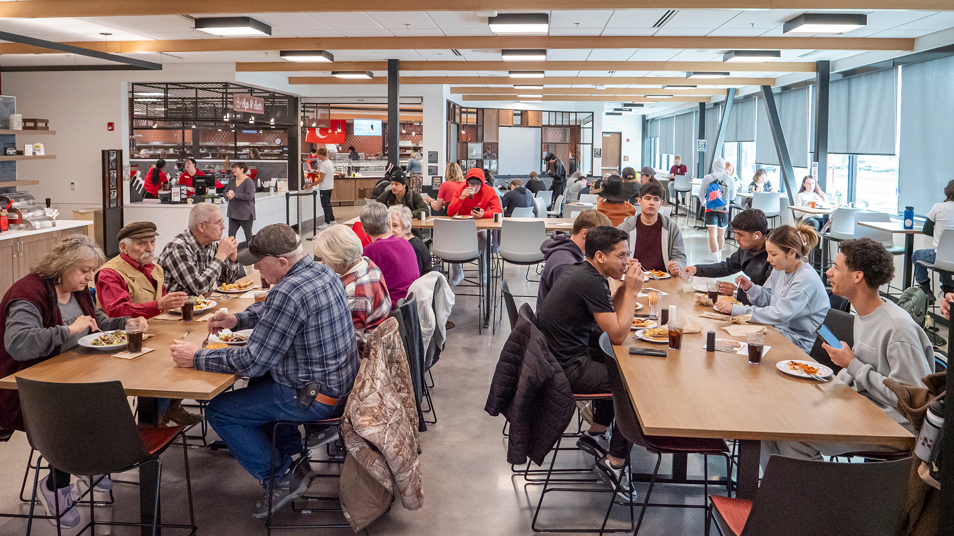A goup of people sitting around tables and eating lunch in the college dining hall
